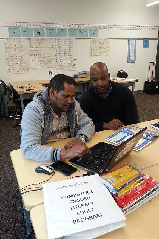 Two men working on a laptop together in a classroom