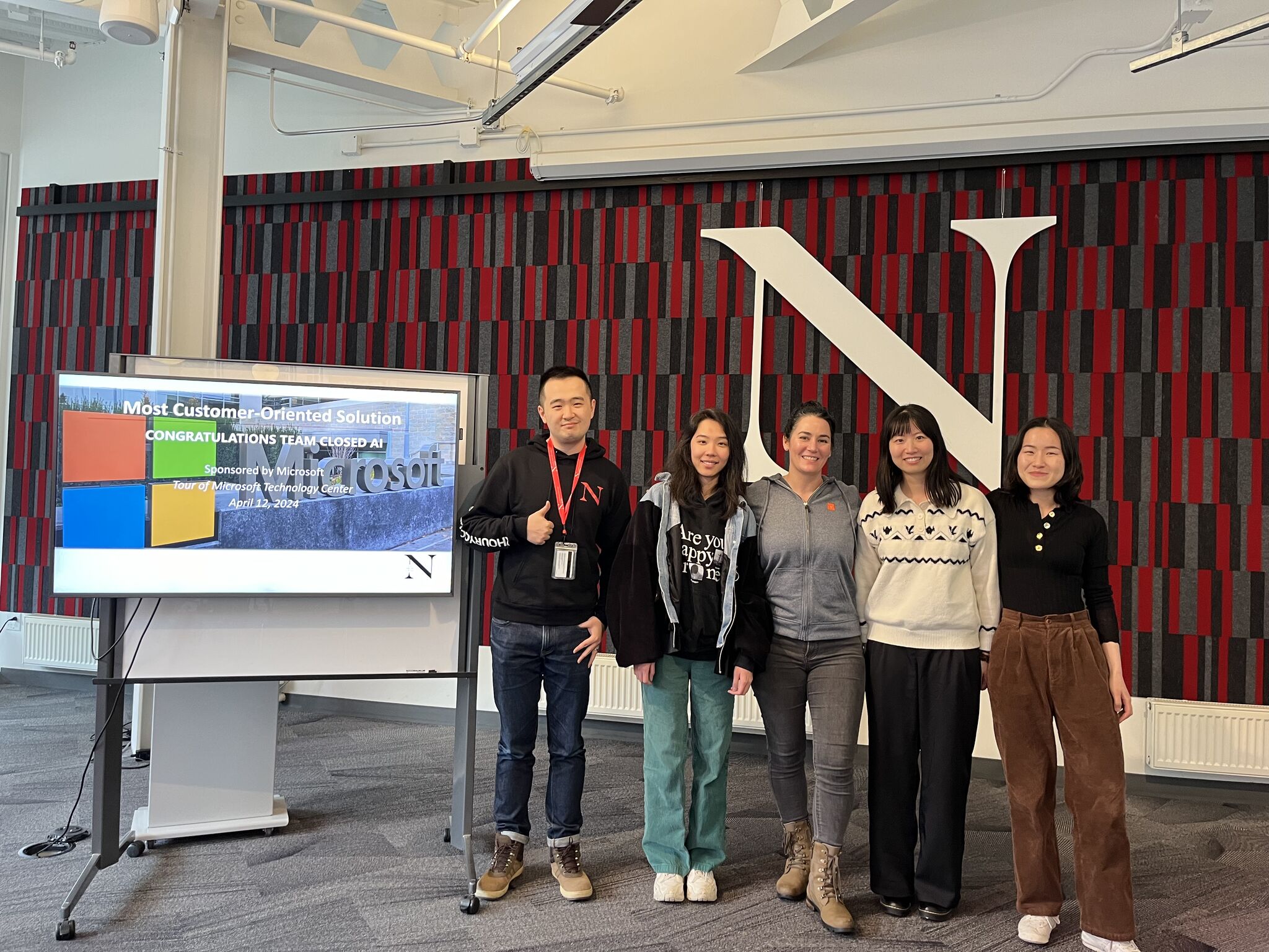 A group of five students smile next to a screen that says "Most Customer-Oriented Solution: Congratulations Team Closed AI"