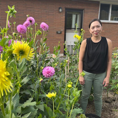 A woman smiles for a photo next to a patch of blooming dahlias