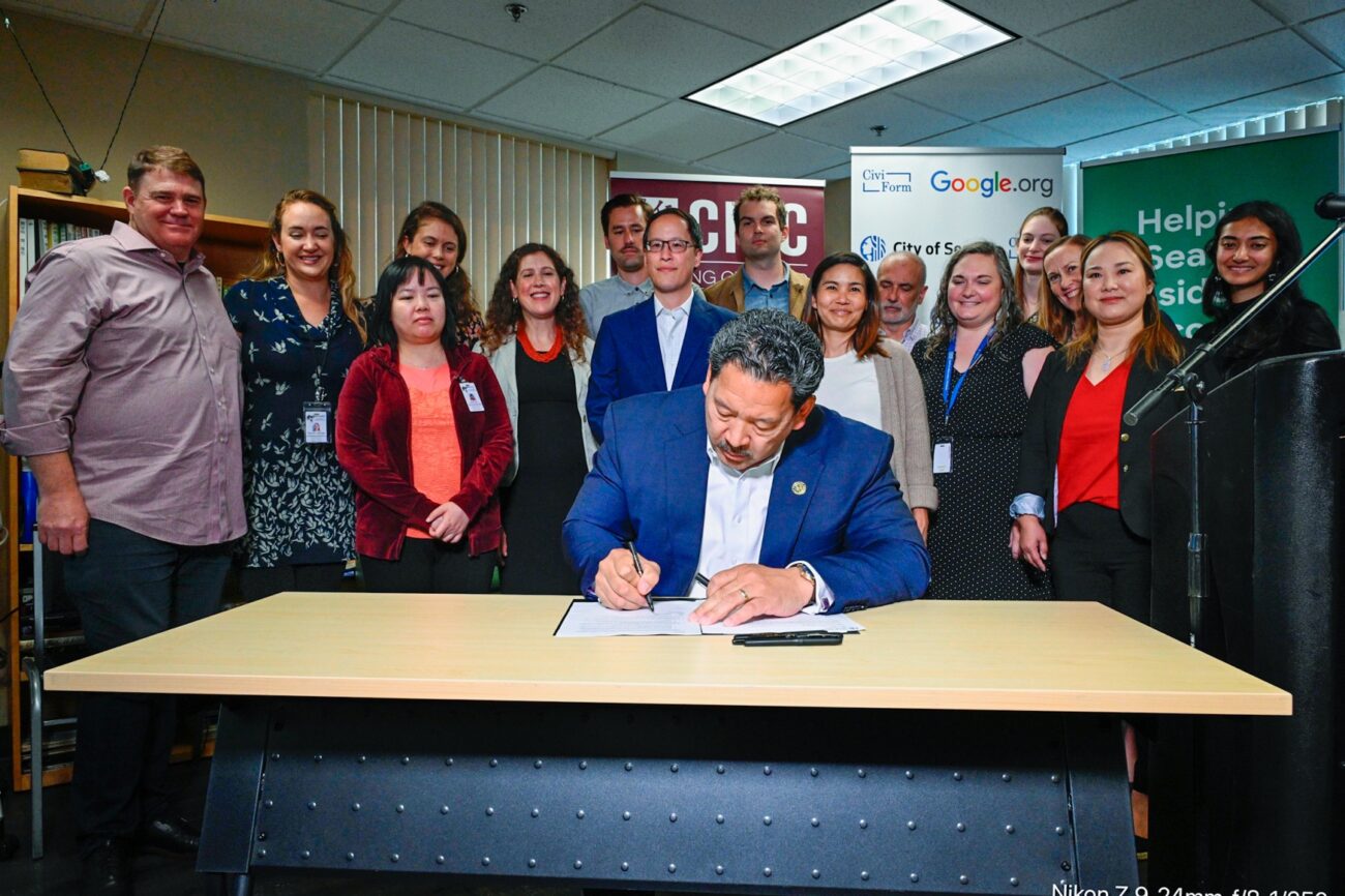 Mayor Harrell signing an Executive Order surrounded by city staff and stakeholders at a press conference