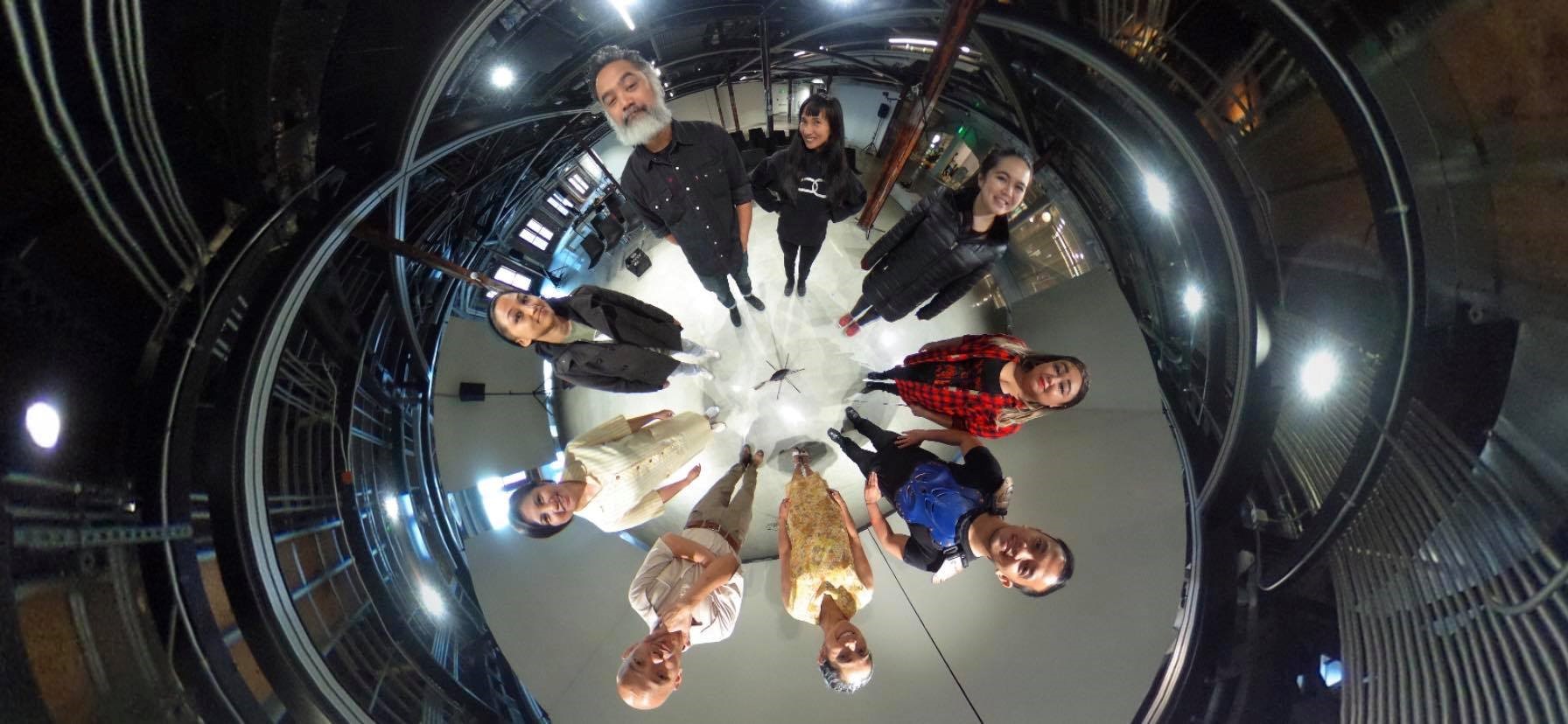 A group of actors standing in a circle, photographed from above as they look up