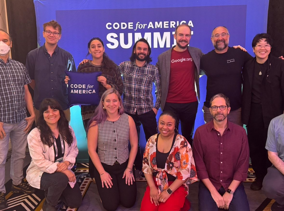 A group of people smiling for a photo in front of a Code for America Summit sign
