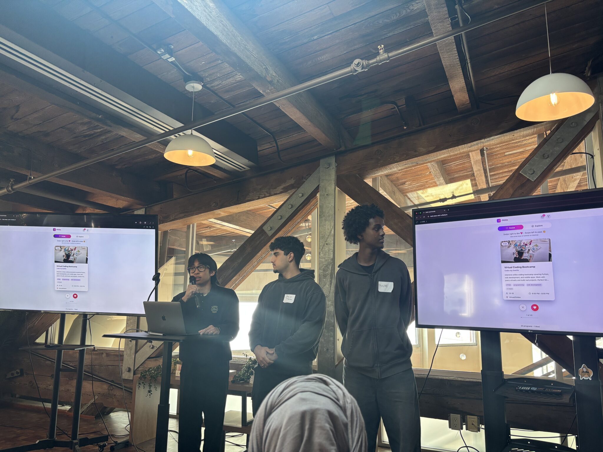 Ryan,  Zobir and Mustaf presenting at a podium with a mockup of their app displayed on the screens behind them