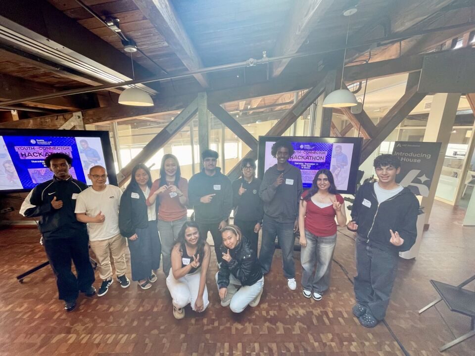A group of 11 young adults smiling and posing for a photo together at Seattle's AI House after the hackathon