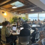 A crowd of participants working on their projects at the Community Innovation Hackathon at the AI House