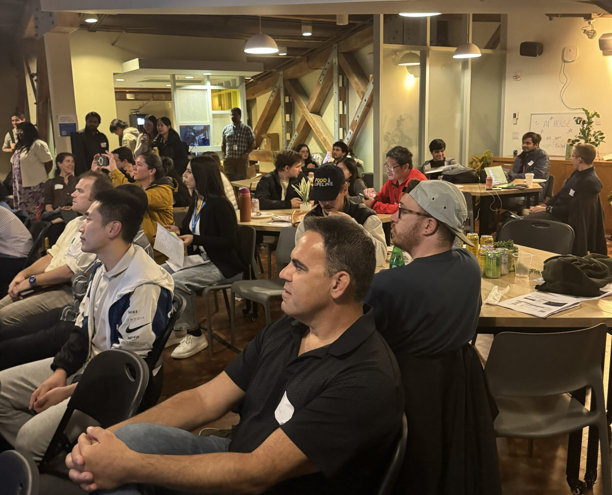 The crowd at the hackathon sitting at tables and chairs, listening to a presentation