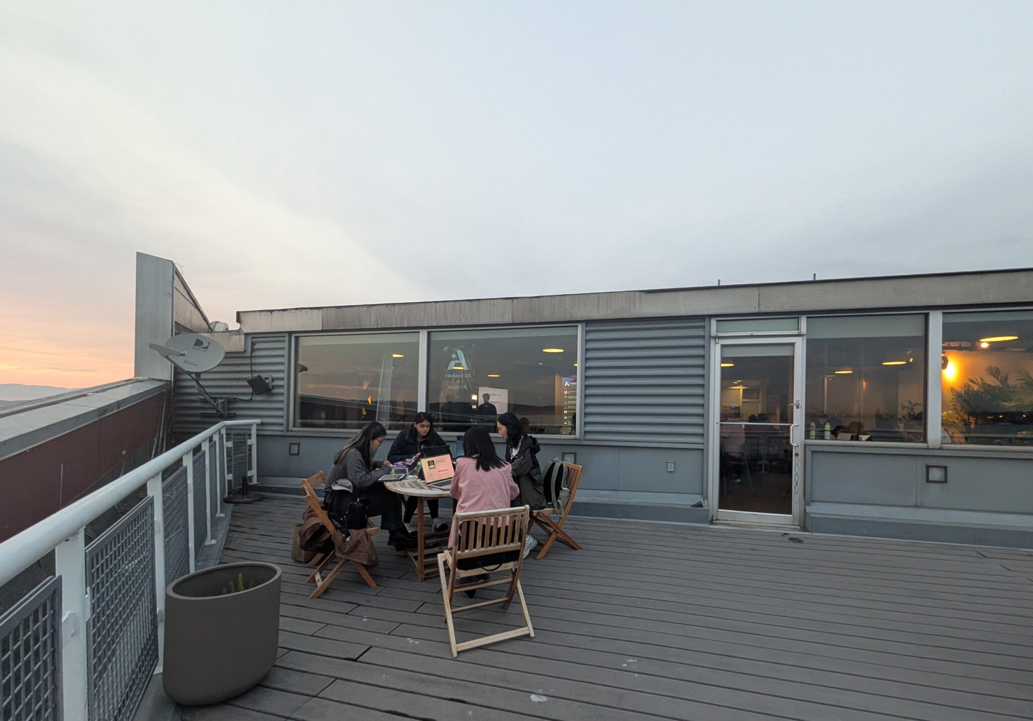 A group of four working on their laptops on a balcony at sunset