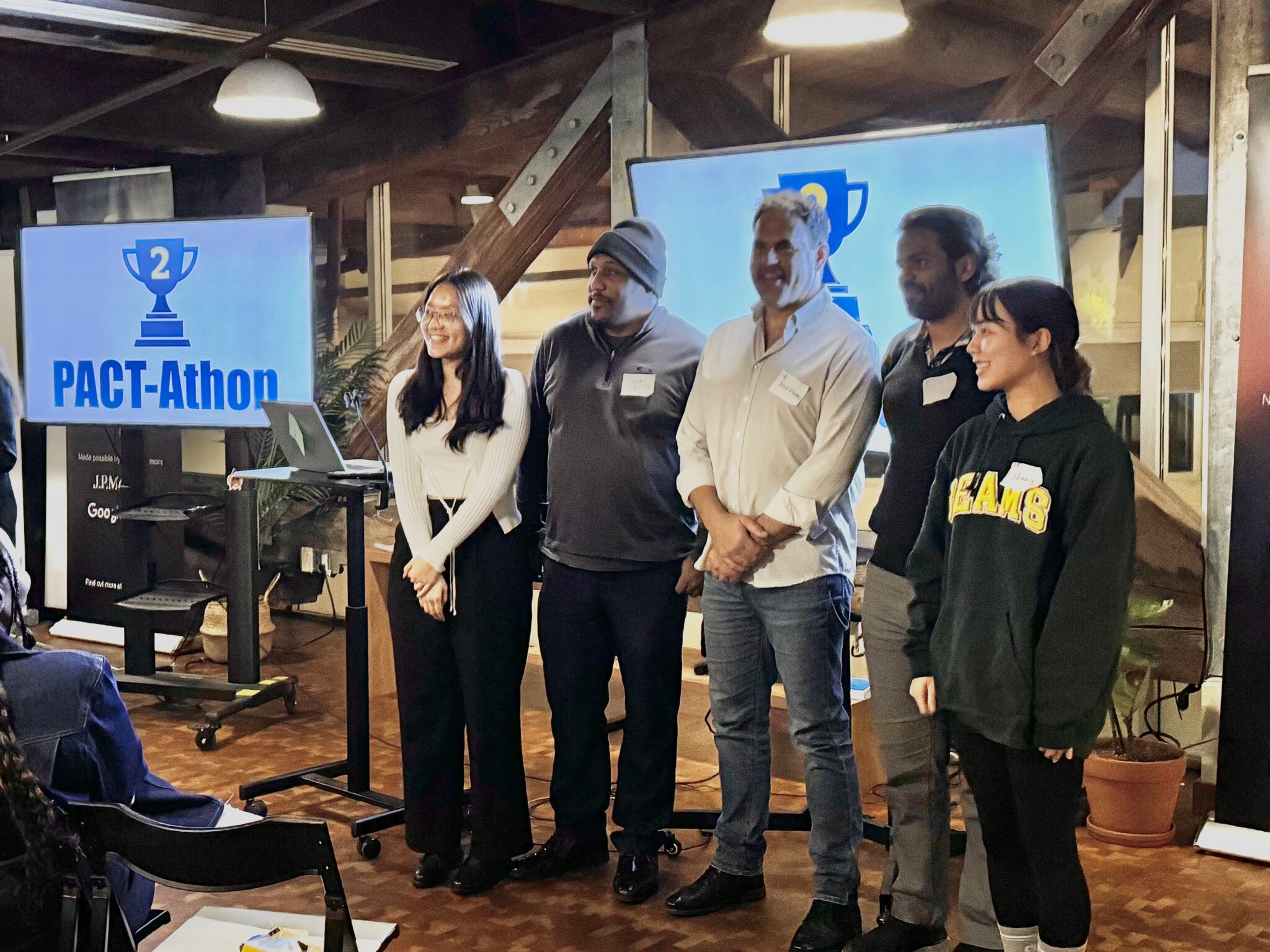 A team of five people poses for a photo in front of a TV displaying a 2nd place trophy image