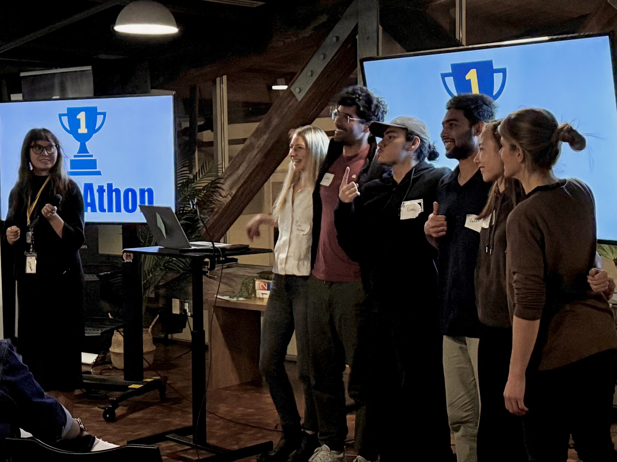 A team of six people poses for a photo in front of a TV displaying a 1st place trophy image