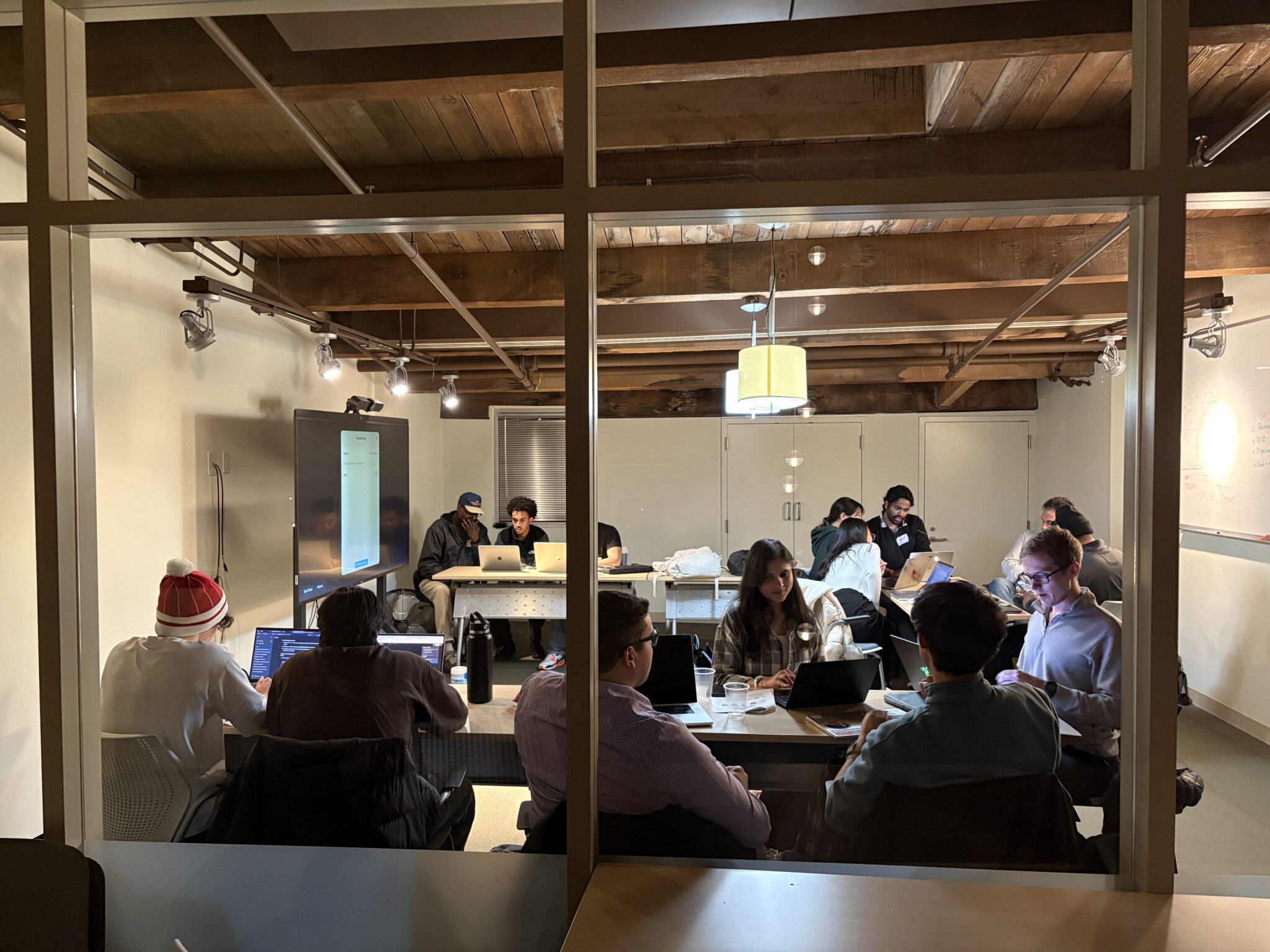 Four hackathon teams sitting in groups and working on their projects in a conference room