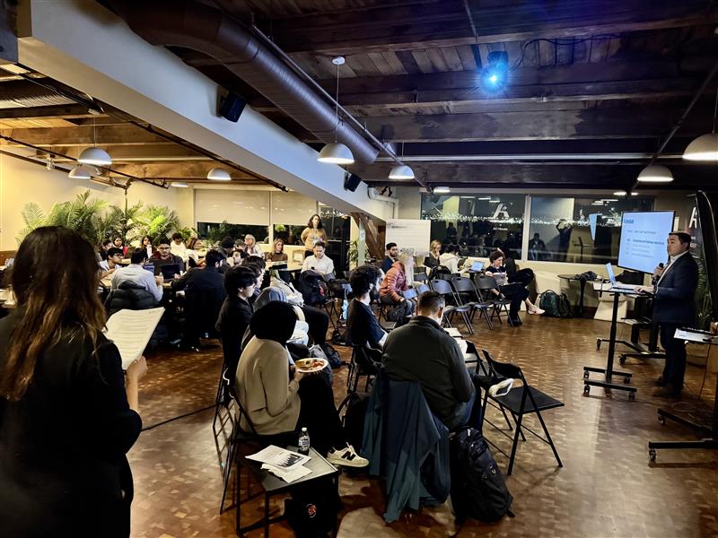 Rob Lloyd speaking at a podium to the crowd of hackathon participants